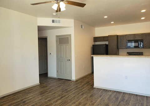 an empty living room with a kitchen and a ceiling fan