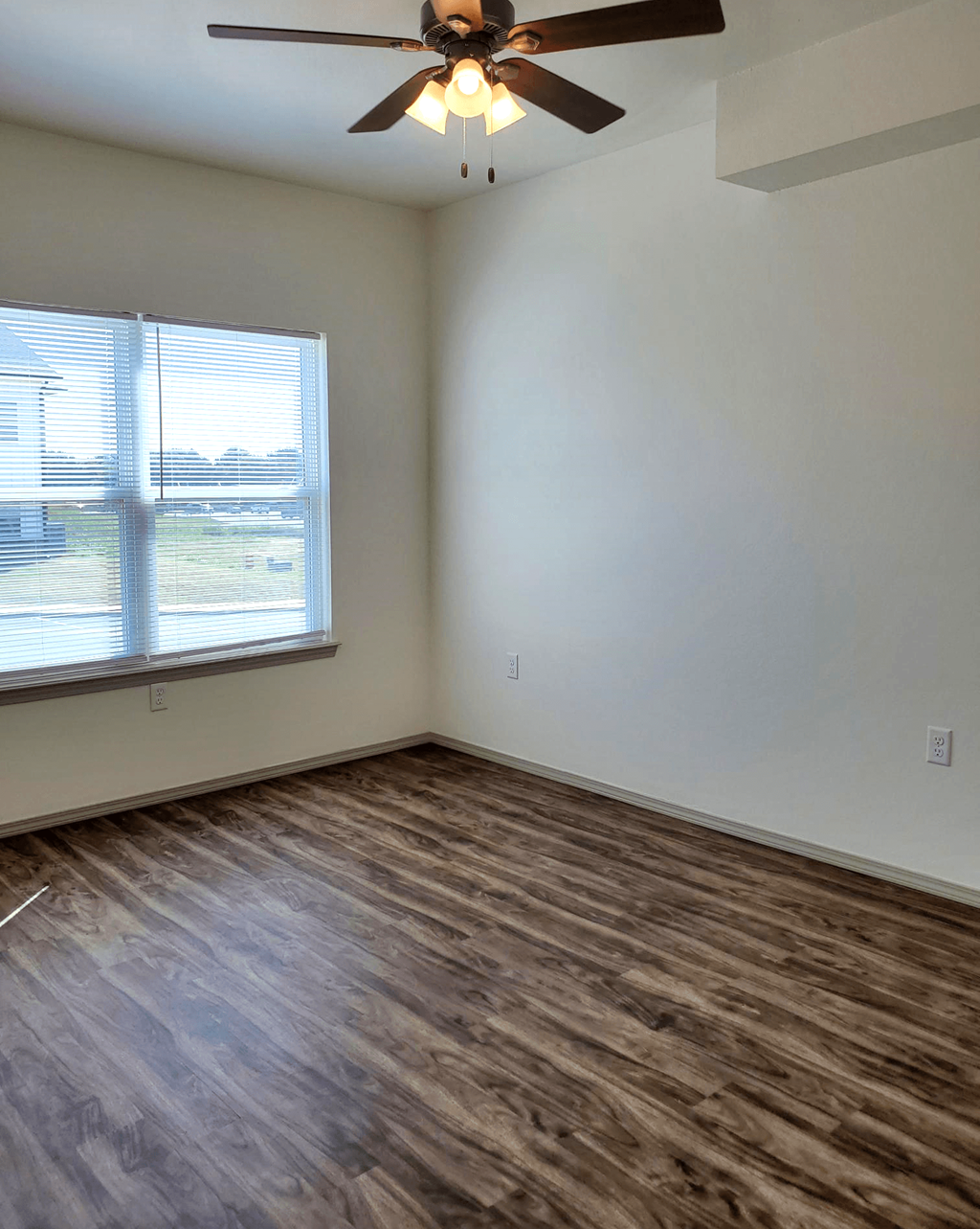 an empty living room with a large window and a ceiling fan