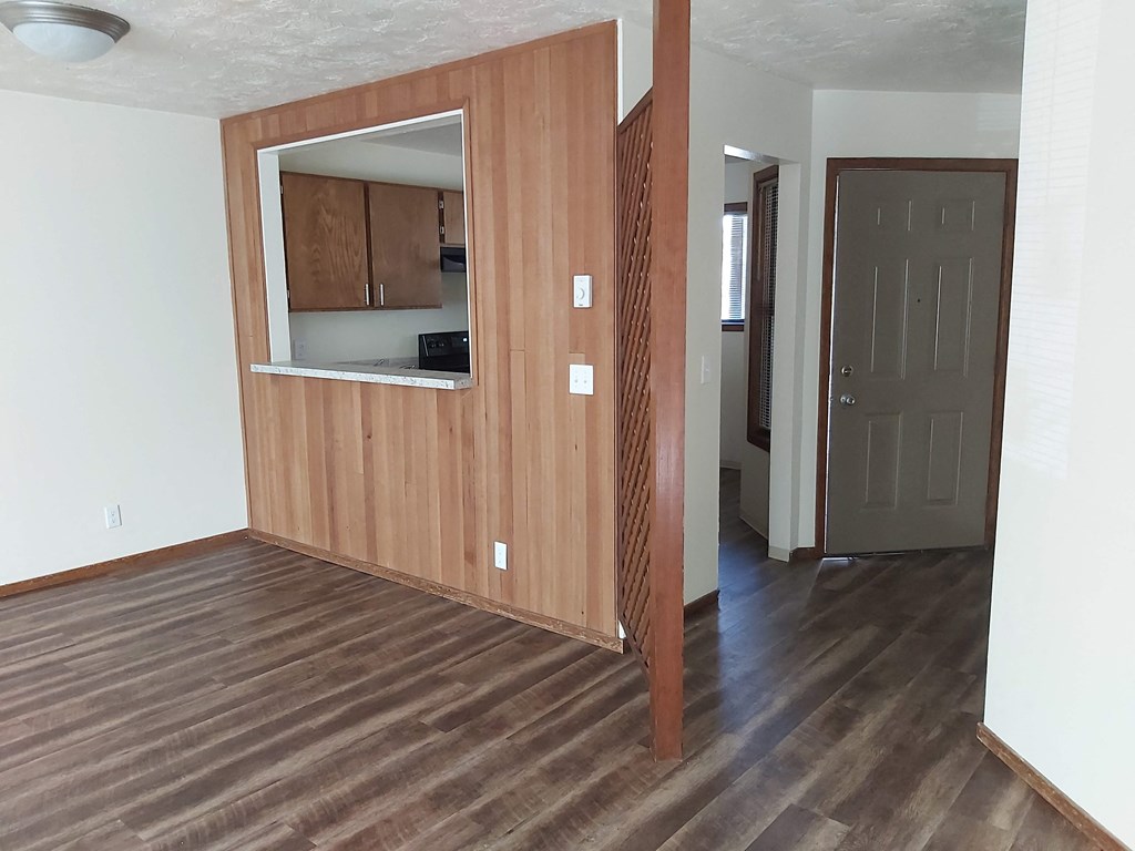 an empty living room with wood flooring and a door to a kitchen
