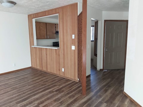 an empty living room with wood flooring and a door to a kitchen