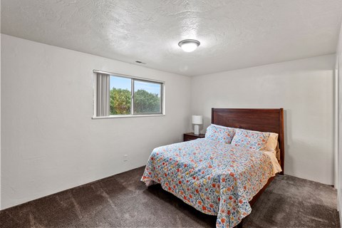 A bedroom with a bed, nightstand, and window.