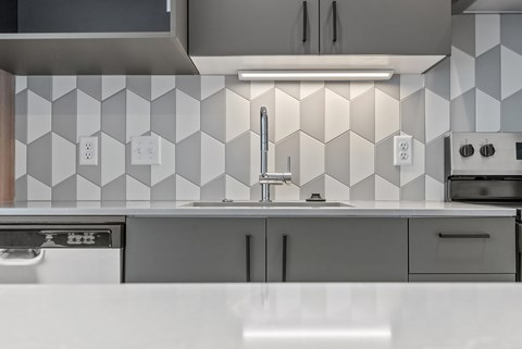 A modern kitchen with a white countertop and a backsplash of white and grey tiles.