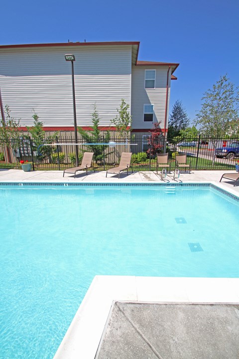 a swimming pool with chairs and a building in the background
