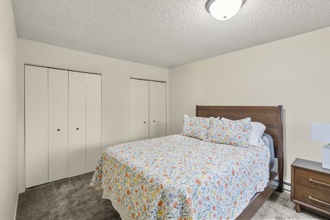 A bedroom with a bed, nightstand, and two closets.