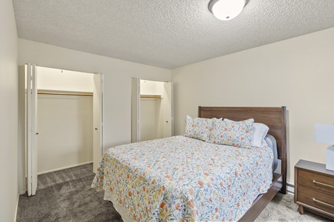 A bedroom with a bed, nightstand, and two closets.