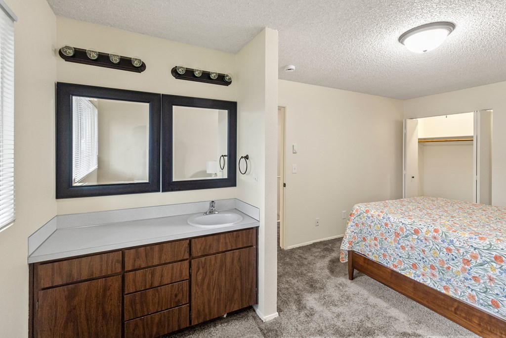 A bedroom with a floral bedspread and a wooden vanity with a mirror above it.