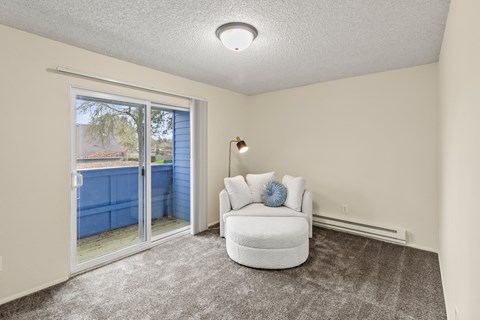 A white chair with a blue pillow is in a room with a sliding glass door.