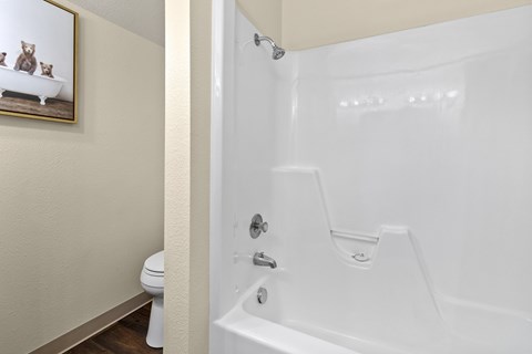 A white bathtub in a bathroom with a toilet and a painting of two dogs on the wall.
