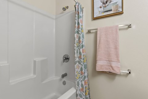 A white bathtub with a floral shower curtain and a pink towel hanging on a towel rack.