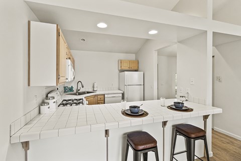 A kitchen with a white tile counter and bar stools.