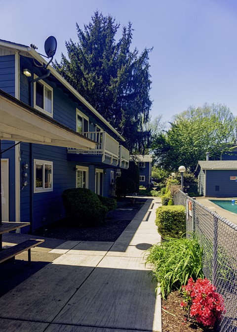 a sidewalk in front of a blue house with a pool