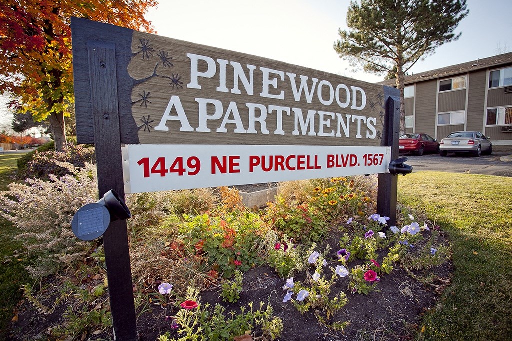 a sign for pinewood apartments in front of a garden