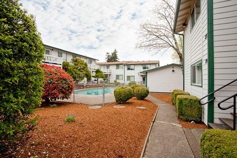 A small garden with a red mulch and a pool in the background.