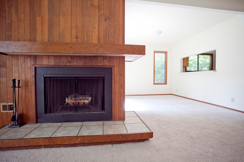 an empty living room with a fireplace with a wooden mantle