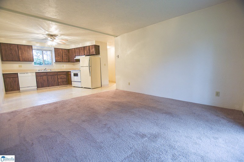 an empty living room with a kitchen and a ceiling fan