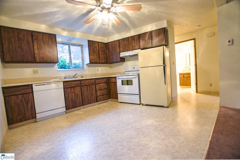 an empty kitchen with white appliances and wooden cabinets