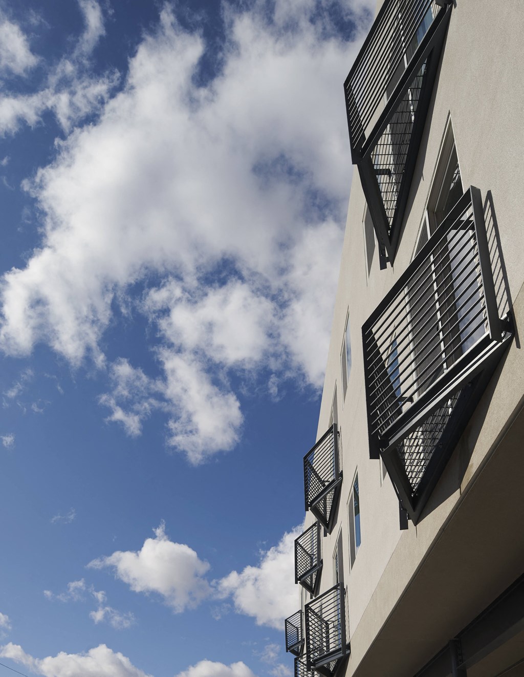 a white building with black balconies against a cloudy blue sky