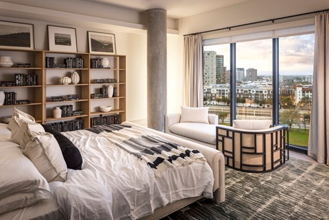 A bedroom with a large bed, a chair, and a bookshelf with various books and decorative items.