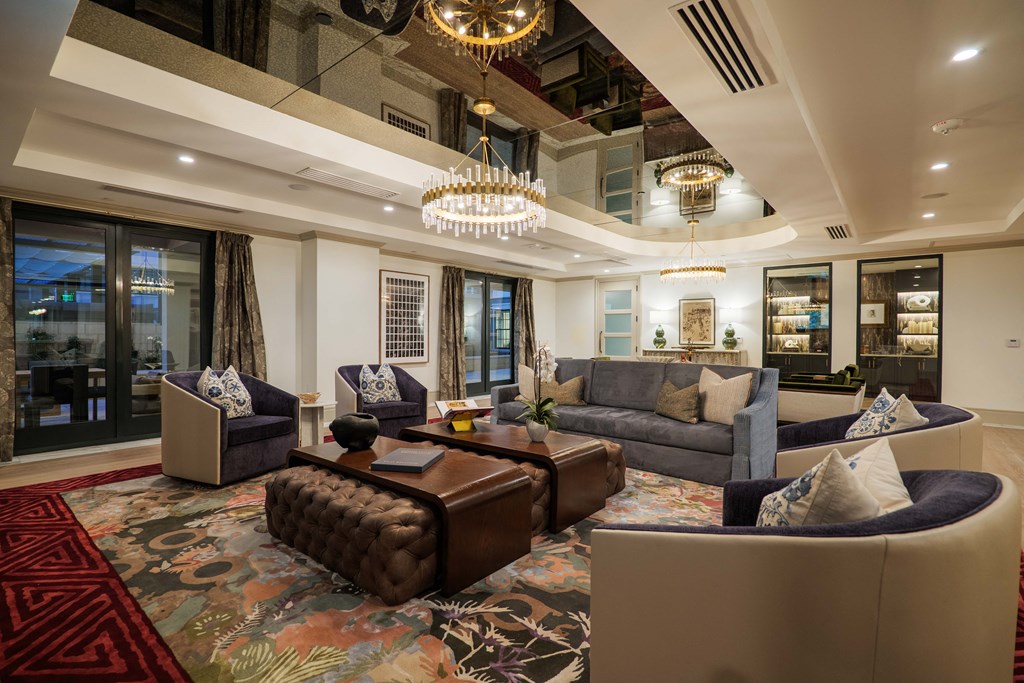 A living room with a brown leather ottoman and a chandelier hanging from the ceiling.