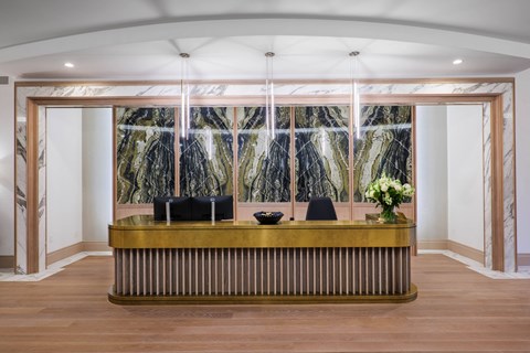 A reception desk with a gold top and a framed picture of a forest behind it.
