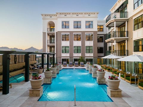 A large swimming pool is surrounded by potted plants and lounge chairs.