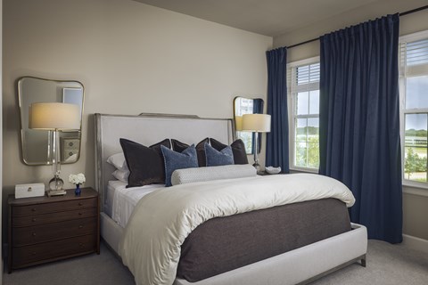A bedroom with a large bed, a nightstand with a lamp, and a window with blue curtains.