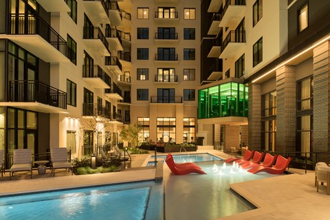 A modern apartment complex with a pool and lounge chairs.