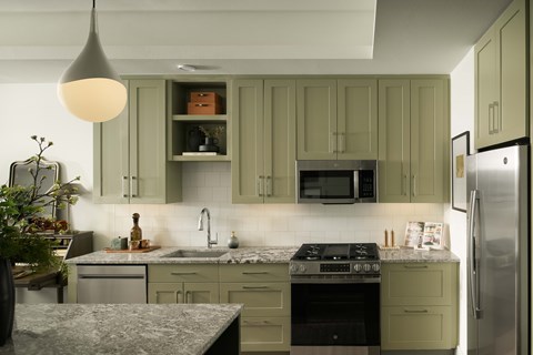 A kitchen with green cabinets and a stainless steel refrigerator.