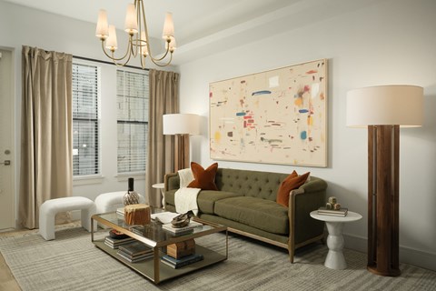 A living room with a green couch, a glass coffee table, and a large abstract painting on the wall.