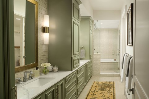 A bathroom with green cabinets and a gold framed mirror.