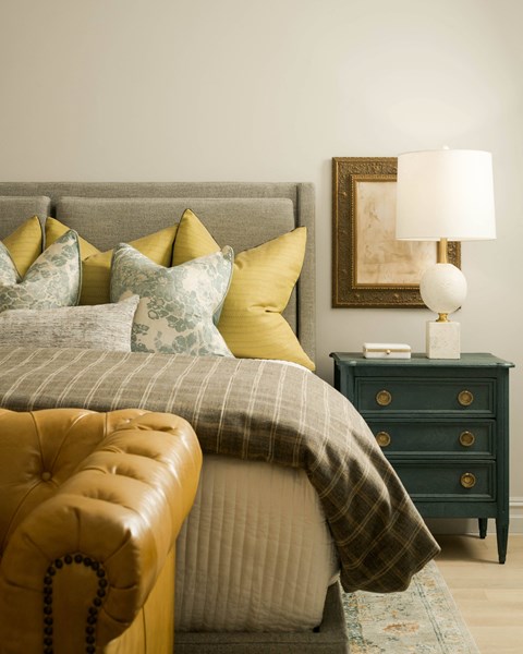 A bed with a yellow headboard and a green nightstand with a white lamp on it.