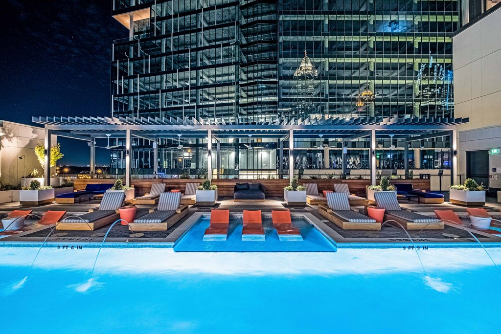 a pool with lounge chairs next to a skyscraper at night