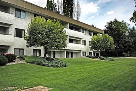 the exterior of a white building with a lawn and trees