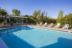 a large swimming pool with chairs and trees in the background
