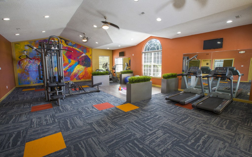 a gym with cardio machines and a colorful painting on the wall