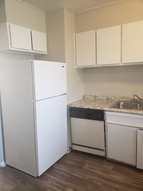 A white refrigerator is in a kitchen with white cabinets.