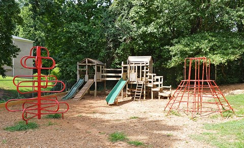 A playground with a red structure, a green slide, and a wooden playhouse.
