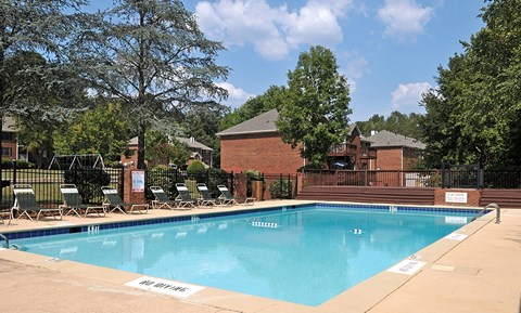 A pool surrounded by trees and chairs.