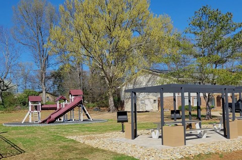 A playground with a red slide and a wooden swing set.