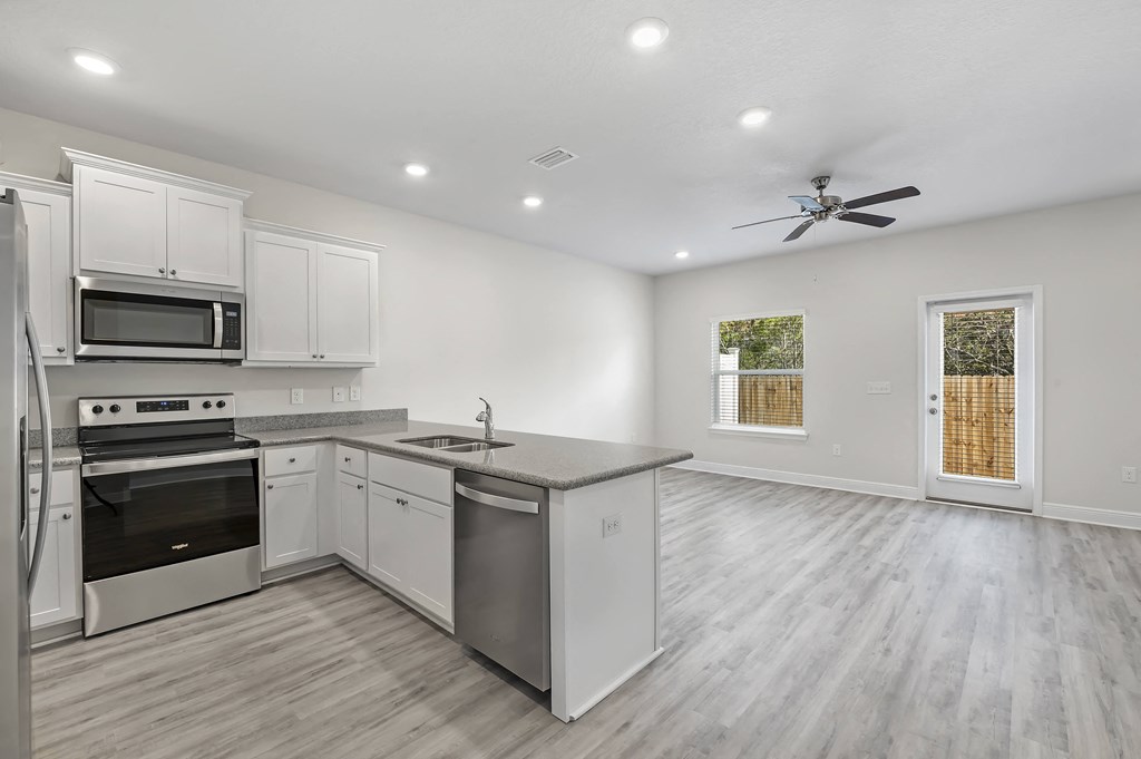 a kitchen and living room with white walls and a ceiling fan