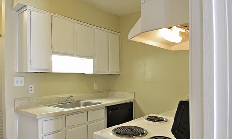 A kitchen with a white stove top oven and white cabinets.
