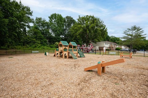 A playground with a seesaw and a slide in the foreground and a building in the background.
