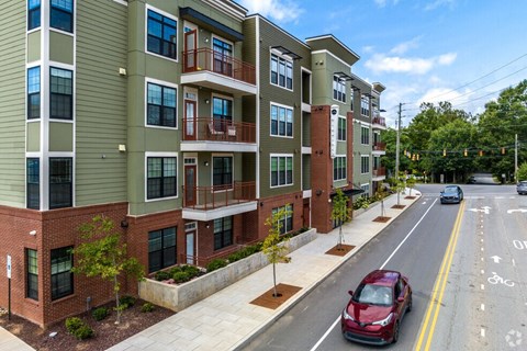 A red car is parked on the side of a street in front of a building.