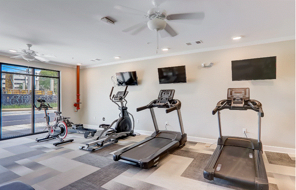 A gym with treadmills, exercise bikes, and a television.