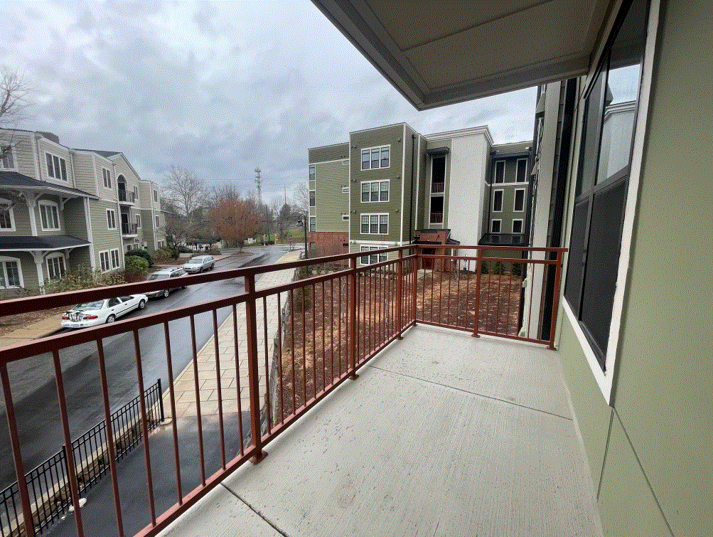 A balcony with a red railing overlooks a street with cars and buildings.