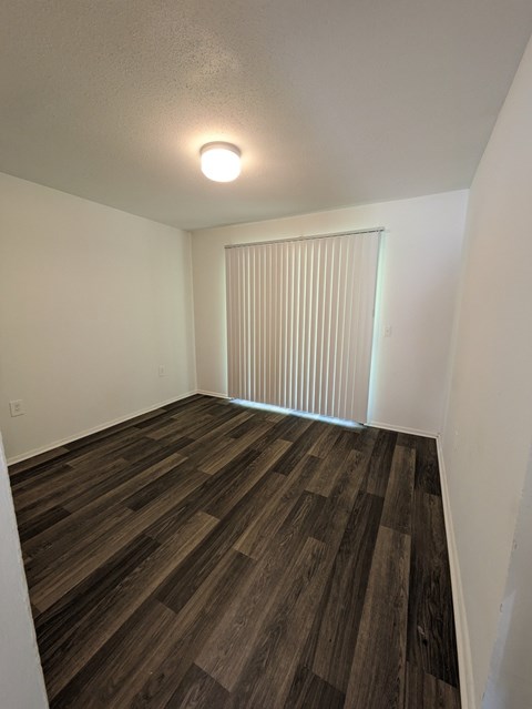 A room with wooden flooring and a window with blinds.