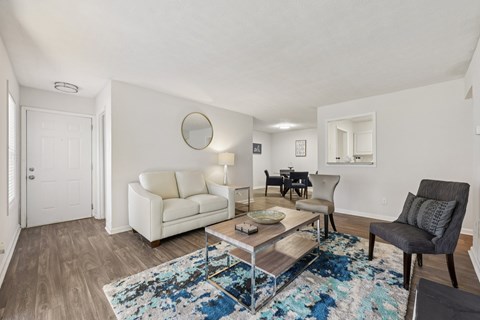 A living room with a white couch, a grey armchair, and a coffee table with a blue rug.