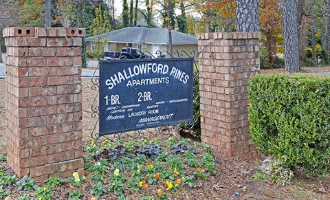 A sign for Shallowford Pines Apartments is displayed in front of a brick wall.