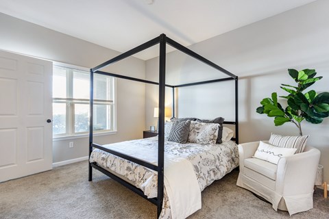 A bedroom with a four poster bed and a white chair.