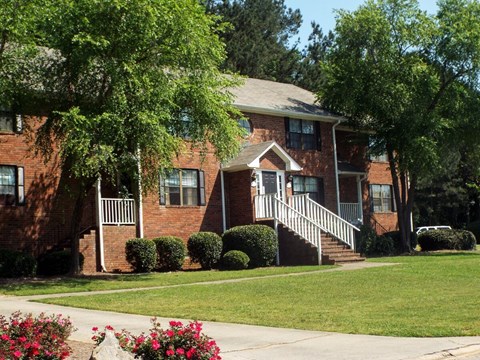 A red brick house with a white porch and a tree in front.